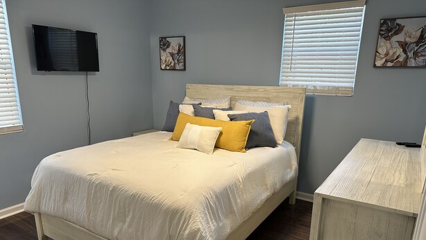A bedroom with a bed, a TV mounted on the wall, and artwork on the walls. - Peaceful Marshside Escape -Family Friendly- Easy Beach Access • Outdoor Living (Hilton Head Island)