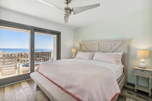 Une chambre dotée d’un grand lit, d’un ventilateur de plafond, d’une table de chevet avec une lampe et offrant une vue sur l’océan grâce à une porte coulissante.