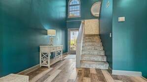 Un pasillo con paredes color turquesa, piso de madera, un banco blanco y una escalera.
