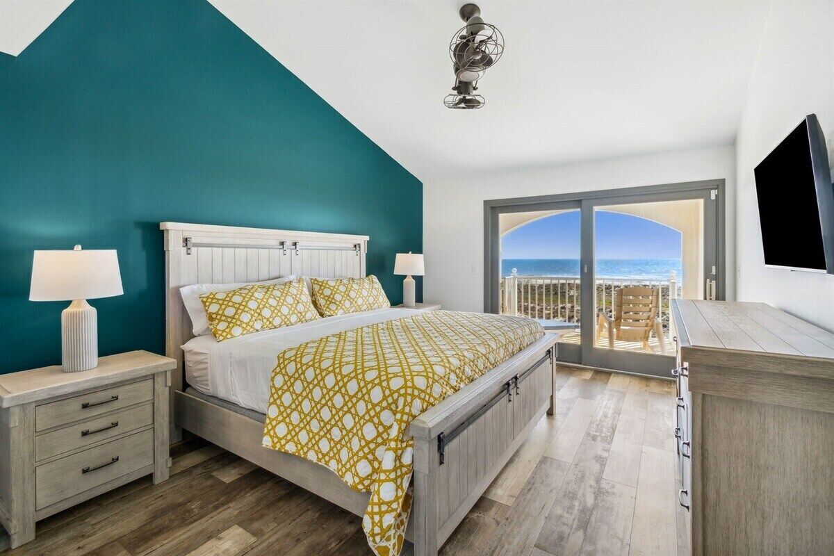 Een slaapkamer met een bed, nachtkastjes, een dressoir en een balkon met uitzicht op zee.
