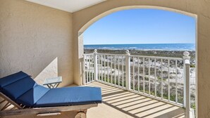 Un balcón con vista a la playa, una silla de lounge y una mesita.