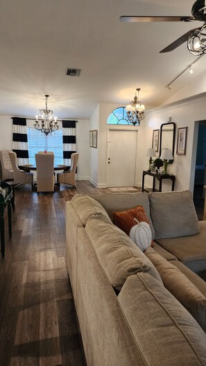 A spacious living room with a large sofa, a dining area with a table and chairs, and a ceiling fan.