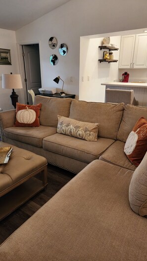 Una sala de estar con un sofá modular, una mesa de centro y una zona de cocina con armarios y encimera.