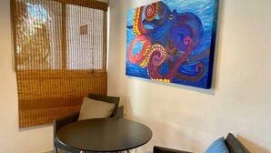 Een kamer met een ronde tafel, twee stoelen, een hanglamp en een groot schilderij aan de muur.