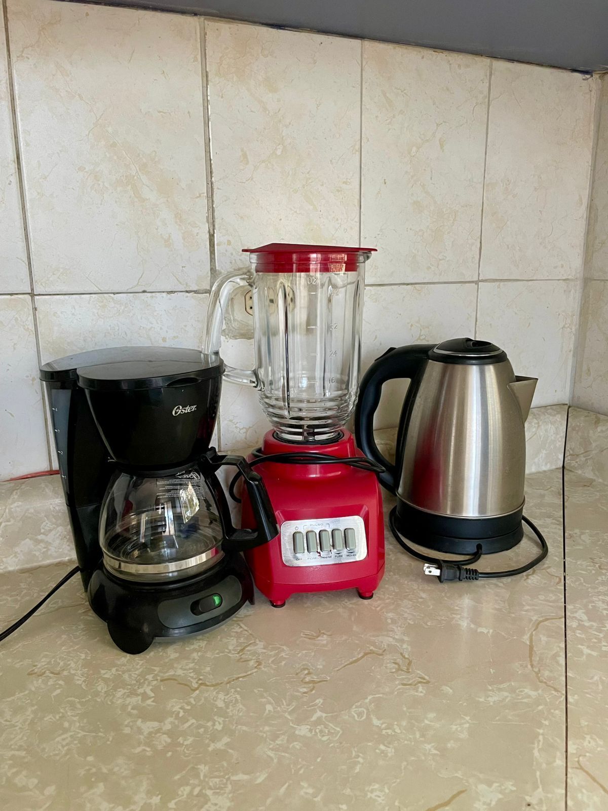 Una cocina con cafetera, licuadora roja y tetera de acero inoxidable sobre una encimera de baldosas.