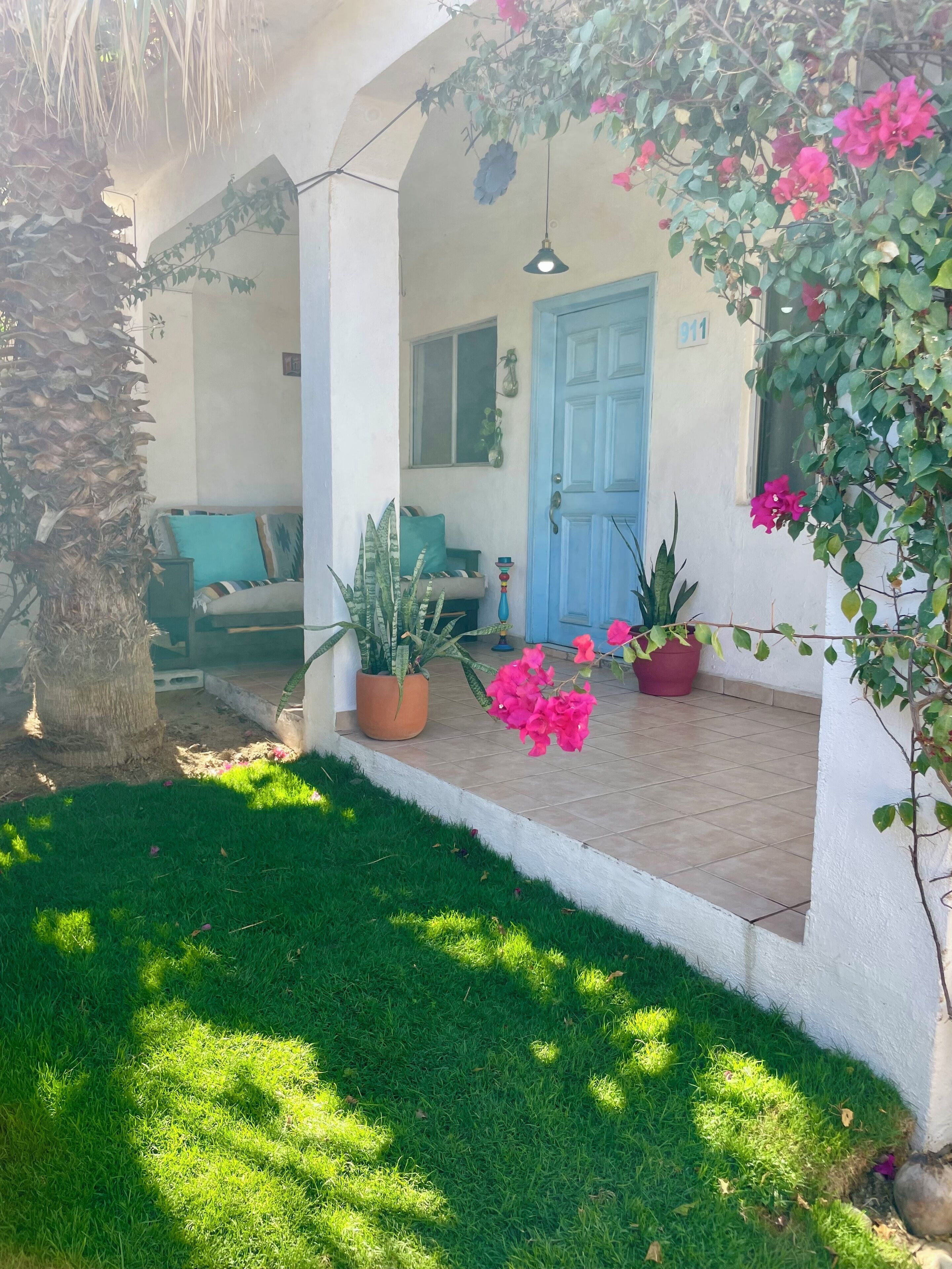 A covered outdoor area with a blue door, potted plants, and a green lawn.