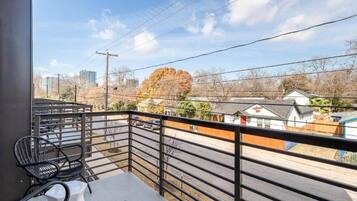 A balcony with a view of a street, a few parked cars, and residential buildings.