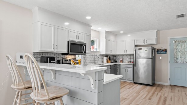 A modern kitchen with white cabinetry, a central island with bar stools, a stainless steel refrigerator, and a microwave. - Short  Walk to beautiful St Joe Bay and Historic downtown Port St Joe.  (Port St. Joe)