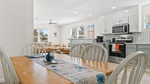 A modern kitchen with white cabinets, a microwave, and an oven. There is a dining table with chairs and a decorative table runner. - Short  Walk to beautiful St Joe Bay and Historic downtown Port St Joe.  (Port St. Joe)