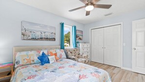 A bedroom with a bed, a ceiling fan, a window with curtains, a dresser, and a door. - Short  Walk to beautiful St Joe Bay and Historic downtown Port St Joe.  (Port St. Joe)