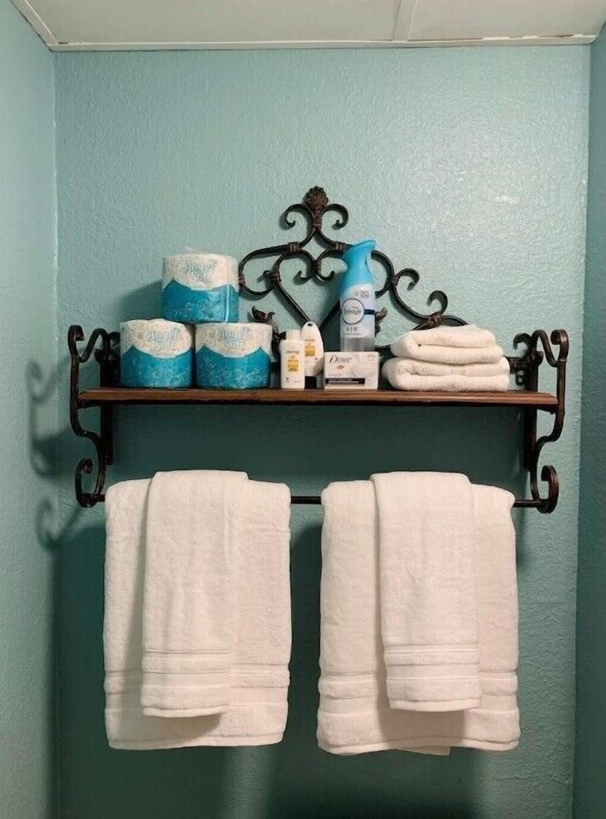 Une salle de bain avec un mur de couleur turquoise, un porte-serviettes en métal et une étagère où sont rangés les articles de toilette et les serviettes.