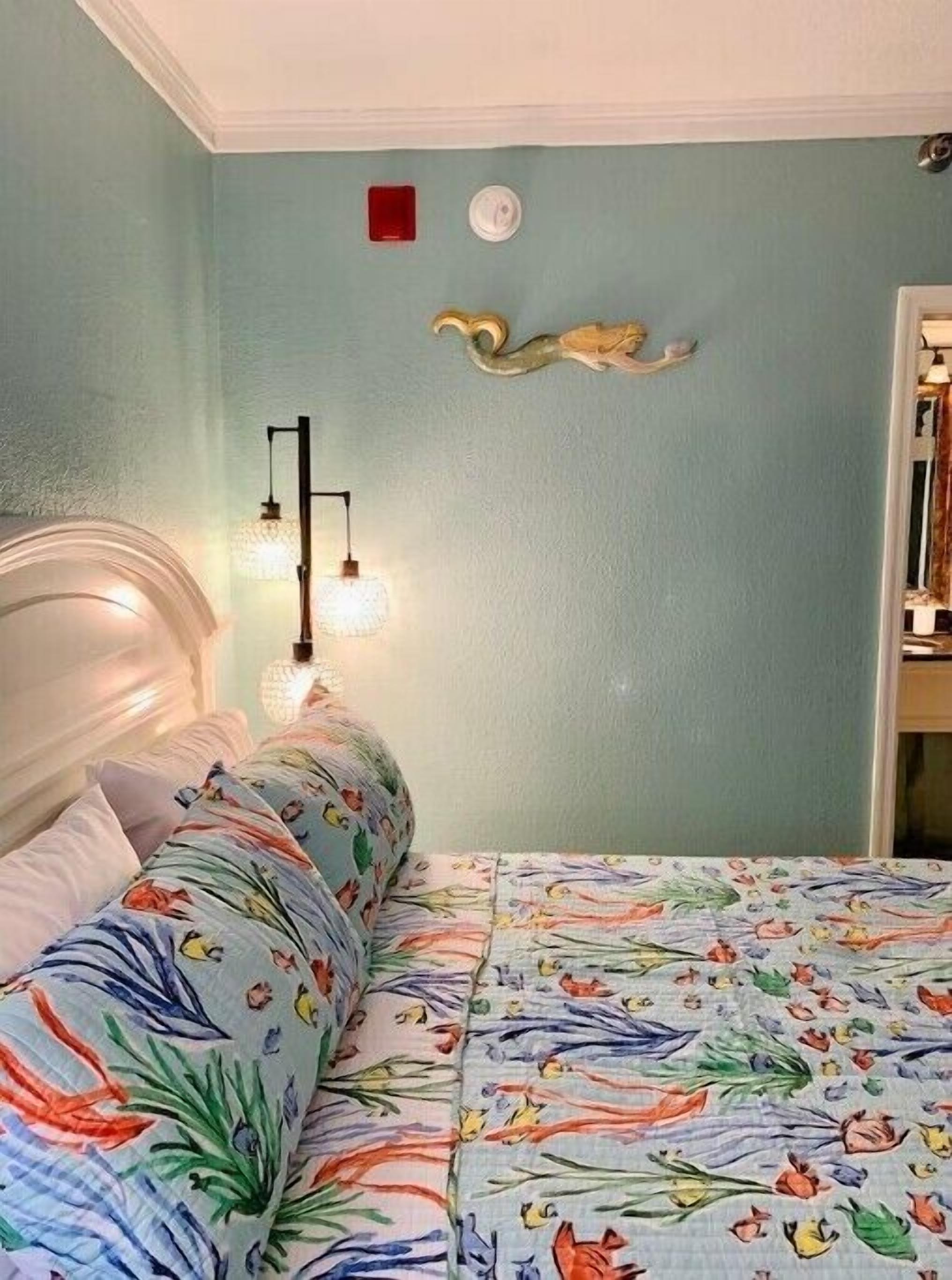 A bedroom with a bed covered in floral bedding, a bedside lamp, and a wall-mounted light fixture.