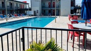 Une piscine avec des chaises longues et un bâtiment à plusieurs étages doté de balcons.