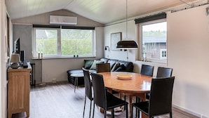 A cozy room with a wooden dining table, black chairs, a black leather sofa, a lamp, and a window with a view of greenery. - Awesome home in Nordborg with kitchen (Nordborg)