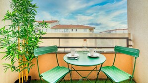 A balcony with a green metal table and chairs, a potted plant, and a clear view of buildings in the background. - Le Verde - Ravissant appartement cosy (Saint-Genis-Laval)