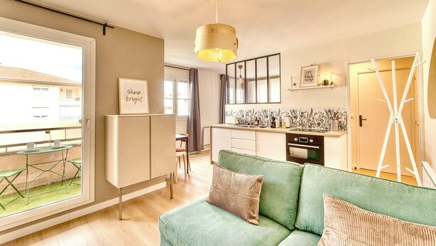 A modern apartment with a green sofa, a kitchen with a built-in oven, and a dining area with a table and chairs. - Le Verde - Ravissant appartement cosy (Saint-Genis-Laval)