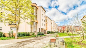 A residential building with multiple balconies, a paved pathway, and a grassy area with benches. - Le Verde - Ravissant appartement cosy (Saint-Genis-Laval)