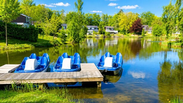 A wooden dock with three blue paddle boats, a calm lake, and houses in the background. - 3 bedroom cozy home in Vlagtwedde (Vlagtwedde)