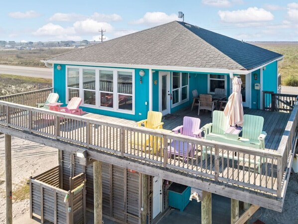 A turquoise beach house with a deck and outdoor seating area.