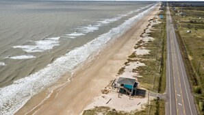 An aerial view of a beach with a road running parallel to the shore, a small building near the beach, and a distant shoreline. - Cabn By the Sea Ultra Secluded Beachfront Home (Bolivar Peninsula)