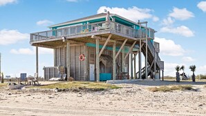 A beach house with a balcony, a lifebuoy, and a staircase leading to the upper level. - Cabn By the Sea Ultra Secluded Beachfront Home (Bolivar Peninsula)