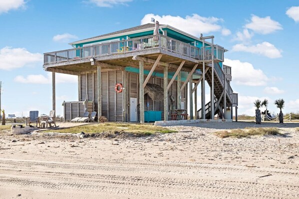 A beach house with a balcony, a lifebuoy, and a staircase leading to the upper level.