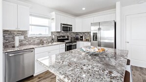 A modern kitchen with white cabinets, stainless steel appliances, and a granite countertop. - Cabn By the Sea Ultra Secluded Beachfront Home (Bolivar Peninsula)