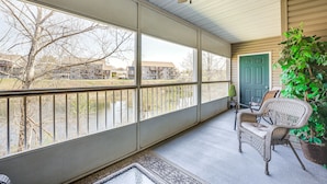 Eine überdachte Veranda mit großen Fenstern, einem Deckenventilator, Korbstühlen und einem Blumentopf.