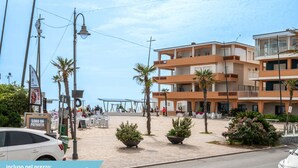 Un bâtiment situé sur la côte, doté de nombreux balcons, d’un espace extérieur aménagé pour s’asseoir et de palmiers.