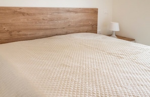 A bed with a wooden headboard, a white lamp on a bedside table, and a plain wall.
