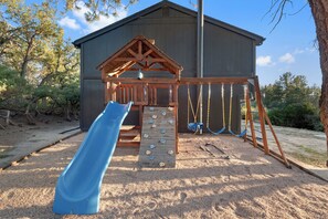 Un parque infantil con tobogán, pared de escalar y columpios.