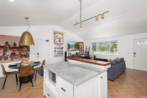 Une cuisine moderne dotée d’un îlot central, d’un coin repas avec des chaises et d’une grande fenêtre qui laisse entrer la lumière naturelle.
