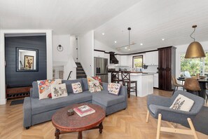 A modern living room with a grey sofa set, a wooden coffee table, and a dining area with a kitchen in the background. - Wilderness Haven with Hot Tub in Franktown (Franktown)