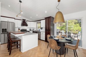 A modern kitchen with a central island, stainless steel appliances, and a dining area with a round table and chairs. - Wilderness Haven with Hot Tub in Franktown (Franktown)