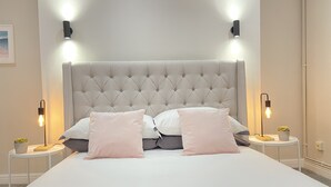 A neatly made bed with a tufted headboard, two bedside tables with lamps, and a small potted plant on each table. - Waimea Apartment 1| Best Location, Beach Front, Parking, Scarborough (North Yorkshire)