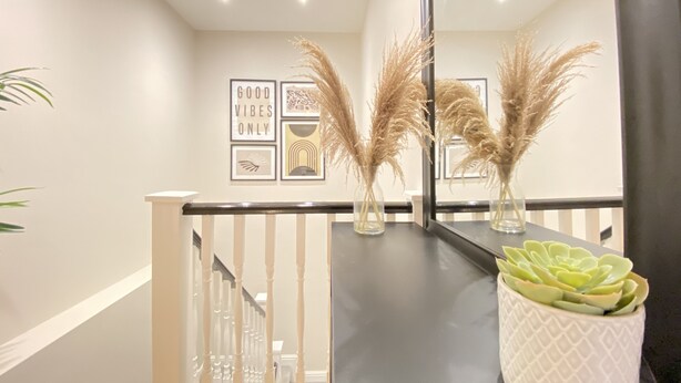 A modern interior with a staircase, a wall with framed artwork, and a potted succulent on a counter. - Waimea Apartment 1| Best Location, Beach Front, Parking, Scarborough (North Yorkshire)