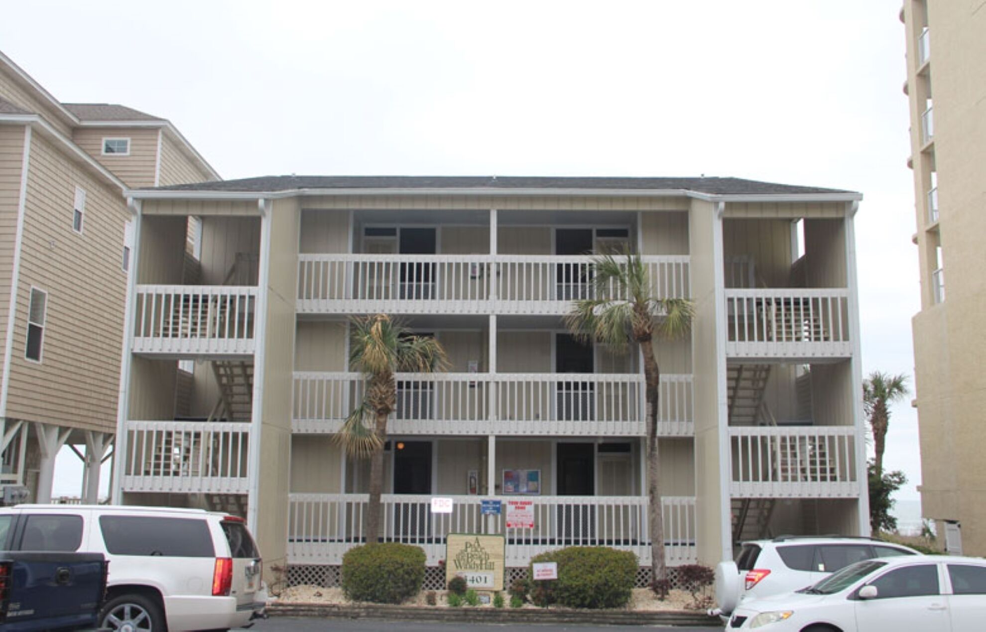 A multi-story hotel with balconies, a parking lot, and a signboard.