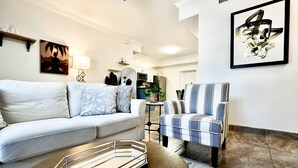 A living room with a sofa, armchair, and coffee table. There are wall art pieces and a kitchen in the background. - SōLE Villa #2|Elegant 2BR Retreat|Beach|Stargazing (Cocoa Beach)