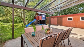 A covered patio with a wooden table and chairs, a blue slide, and a brick wall in the background. - Nice home in Tossens with WiFi (Tossens)