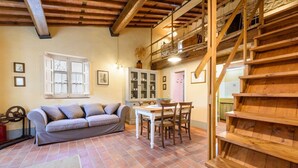 A rustic interior with a sofa, dining table, and wooden staircase.