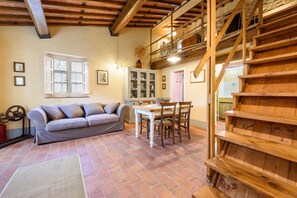 A rustic interior with a sofa, dining table, and wooden staircase.