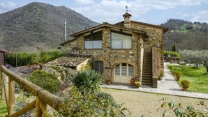 A stone house with a sloped roof, a wooden fence, and a mountainous backdrop.