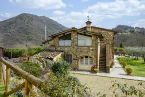 Une maison en pierre avec un toit en pente, une clôture en bois et un paysage montagneux en arrière-plan.