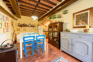 A dining area with a wooden ceiling, a dining table with blue chairs, a cabinet with glass doors, and a tiled floor.