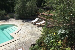 Une piscine entourée de chaises longues, de verdure et d’un dallage en pierre.