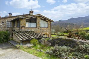 A stone house with a sloped roof, large windows, and a stone staircase leading to the entrance.