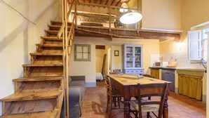 A rustic kitchen with a wooden staircase, a dining table with chairs, and a kitchen counter.
