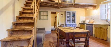 A rustic kitchen with a wooden staircase, a dining table with chairs, and a kitchen counter.