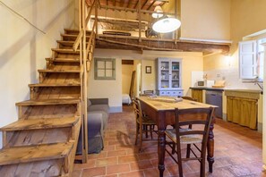 A rustic kitchen with a wooden staircase, a dining table with chairs, and a kitchen counter.