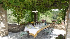 An outdoor dining area with a table set for four, surrounded by stone walls and greenery.